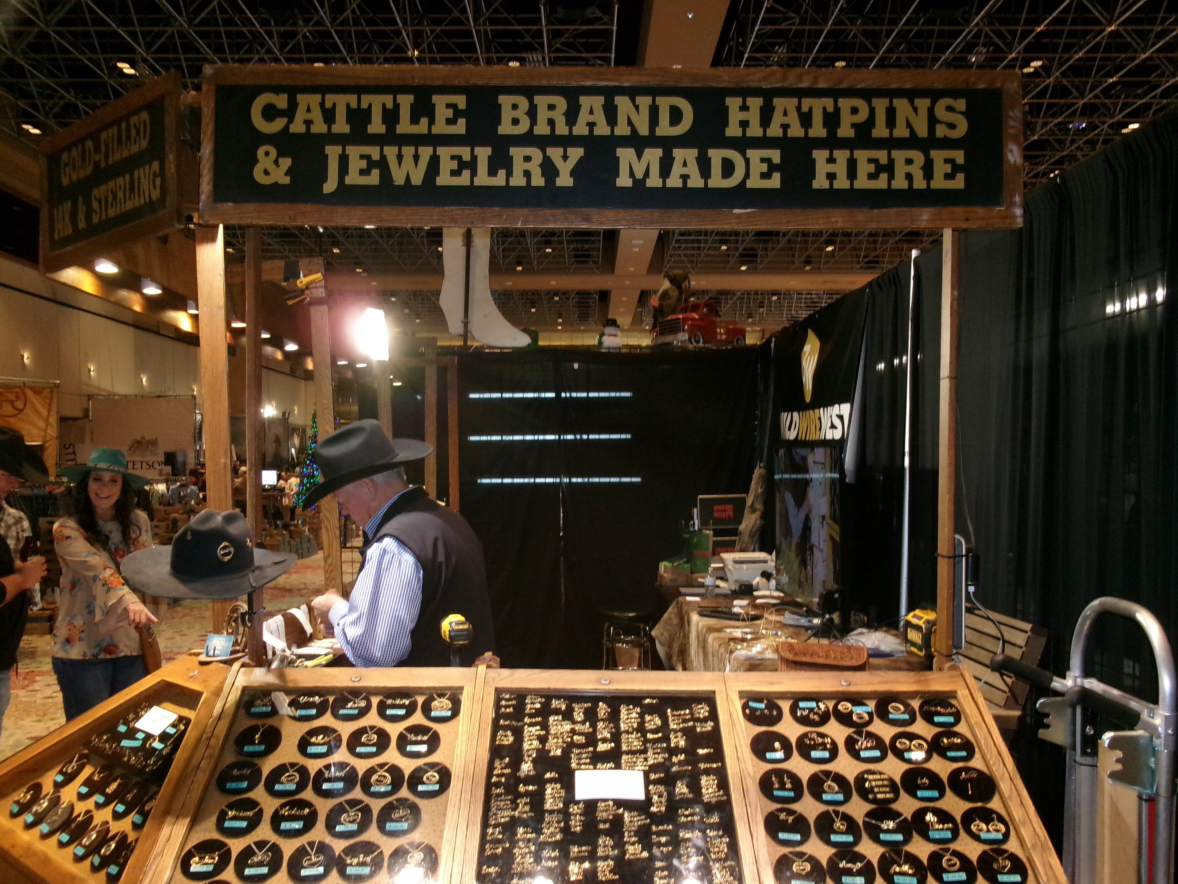 Display of cattle brand hatpins and jewelry with a sign above it in a store setting.