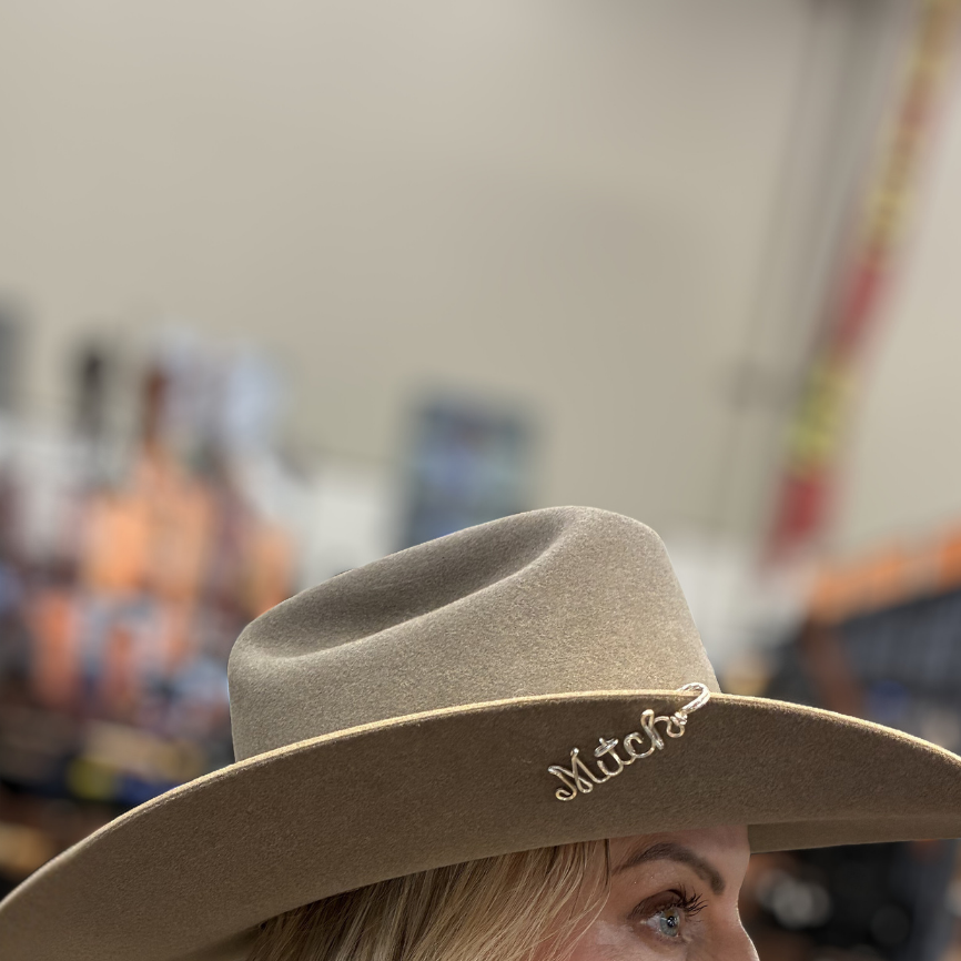 Close-up of a person wearing a beige cowboy hat with 'Mitch' on it, blurred background