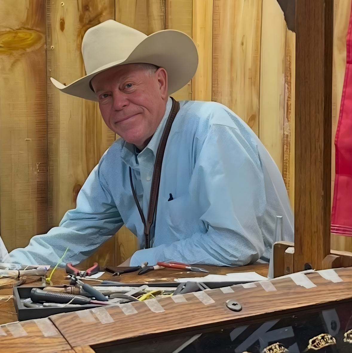 Man wearing a cowboy hat and light blue shirt sitting at a workbench with tools.